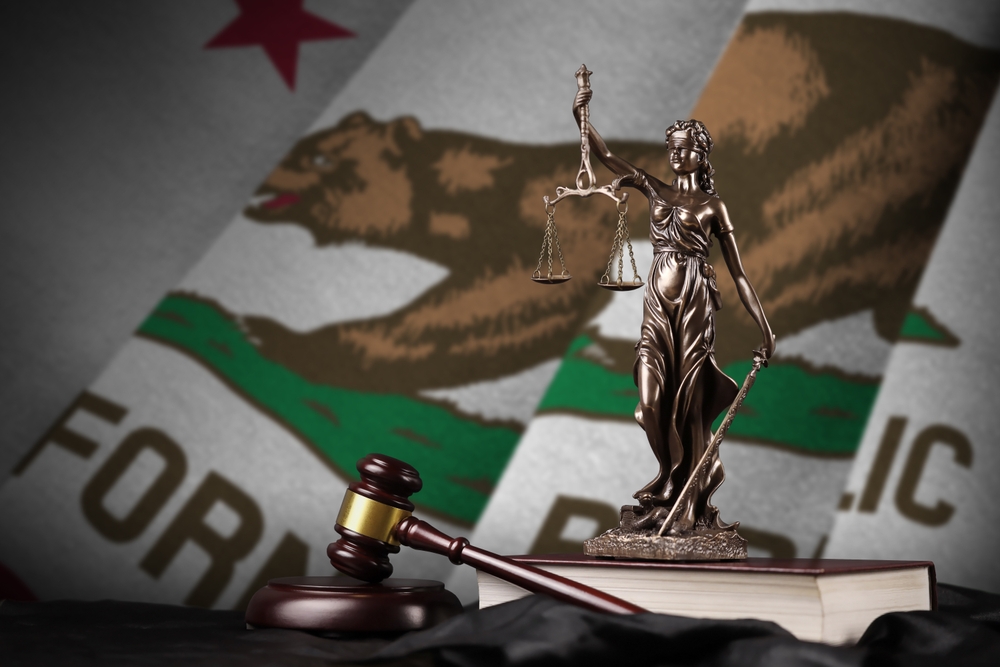 Statue of Justice with scales and a gavel in front of the California flag