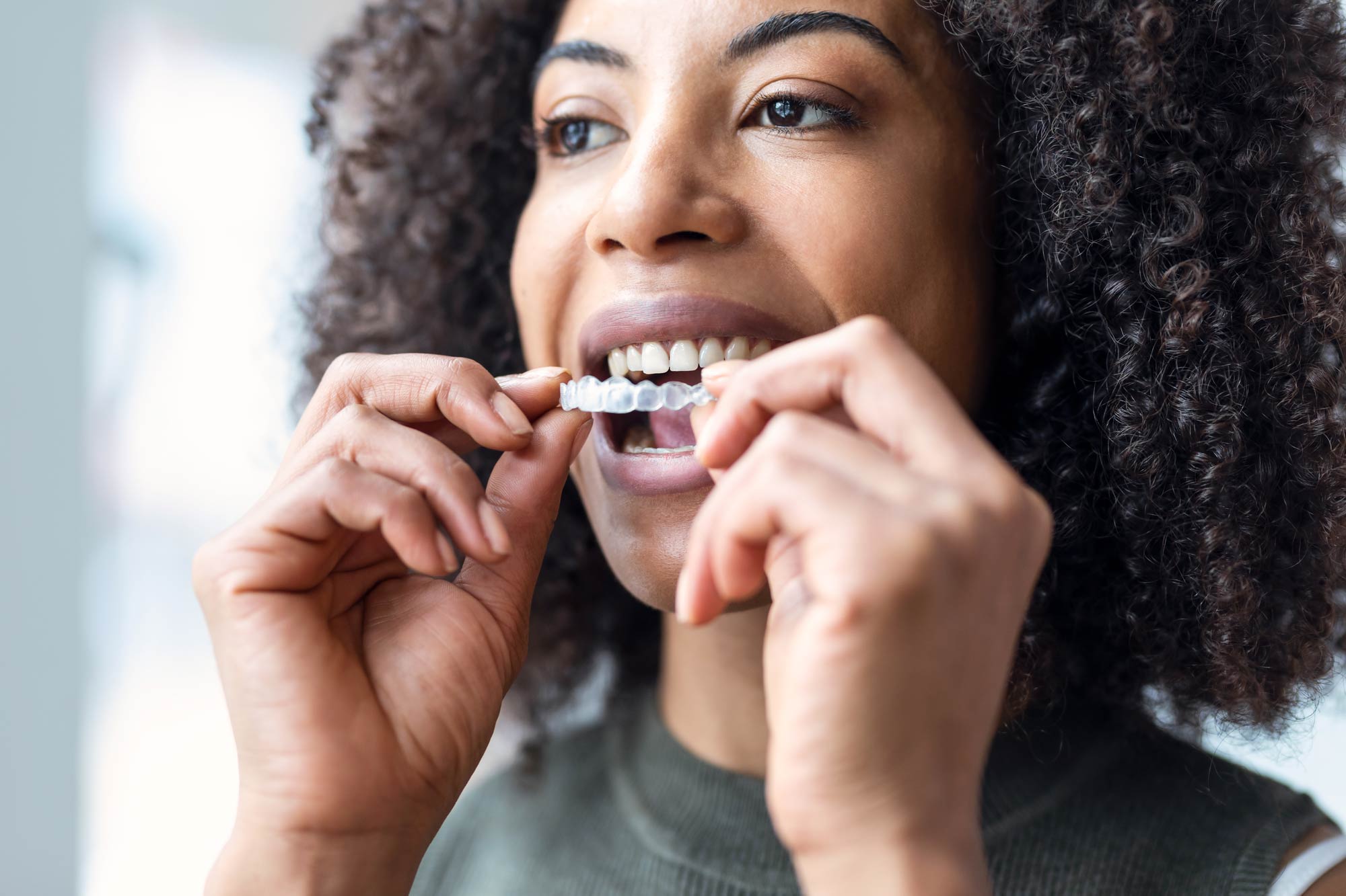 woman placing a clear aligner on her teeth