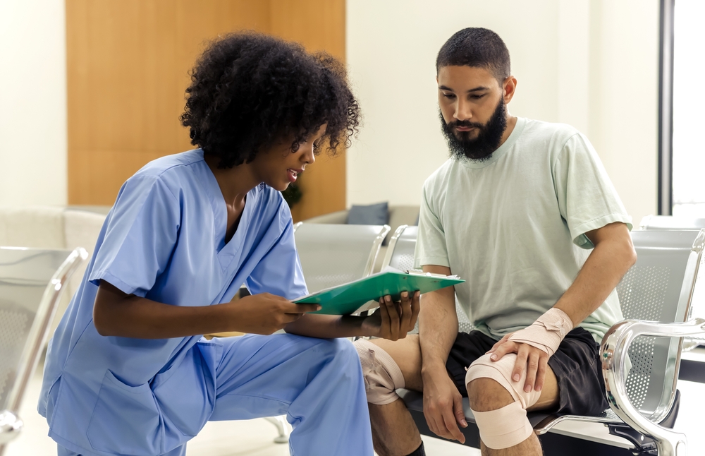 Patient with injured knees and wrists speaking with a physician assistant