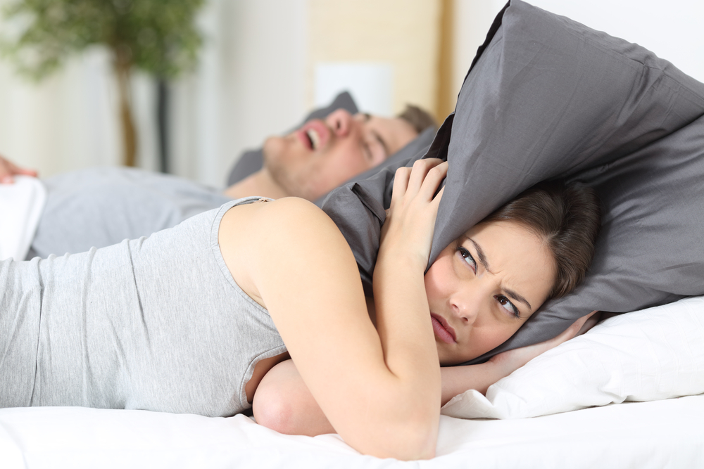 Woman covering ears with pillow because of partner