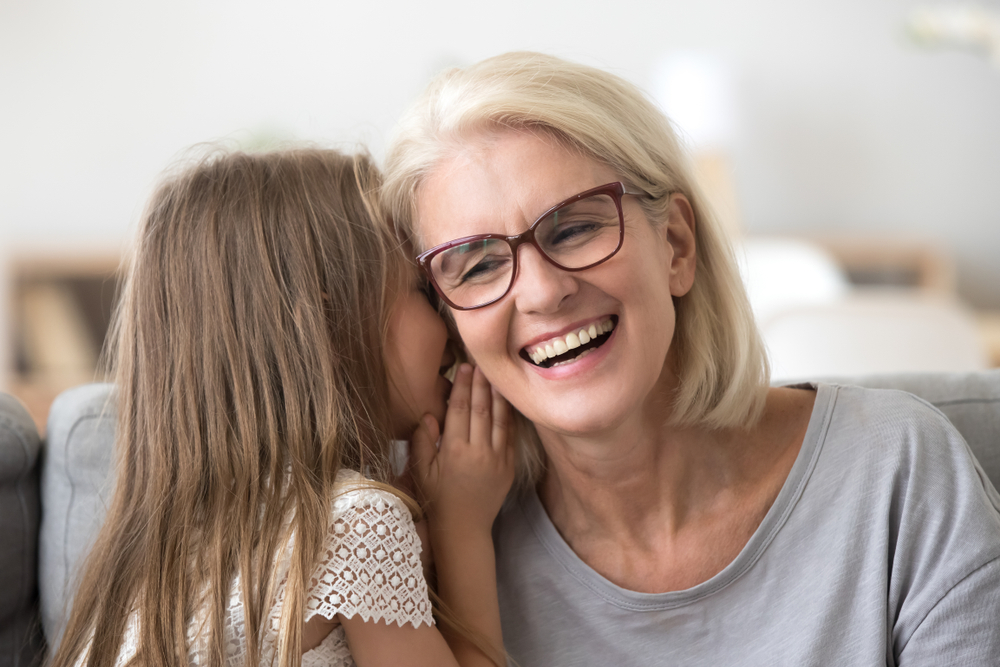 A young girl whispering a secret to her smiling grandmother