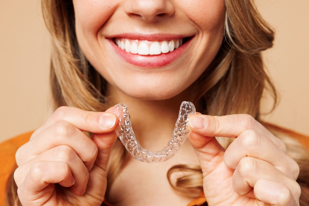 Smiling young woman holding her Invisalign clear aligner