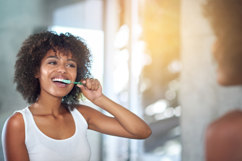 Happy woman brushing teeth while looking the mirror