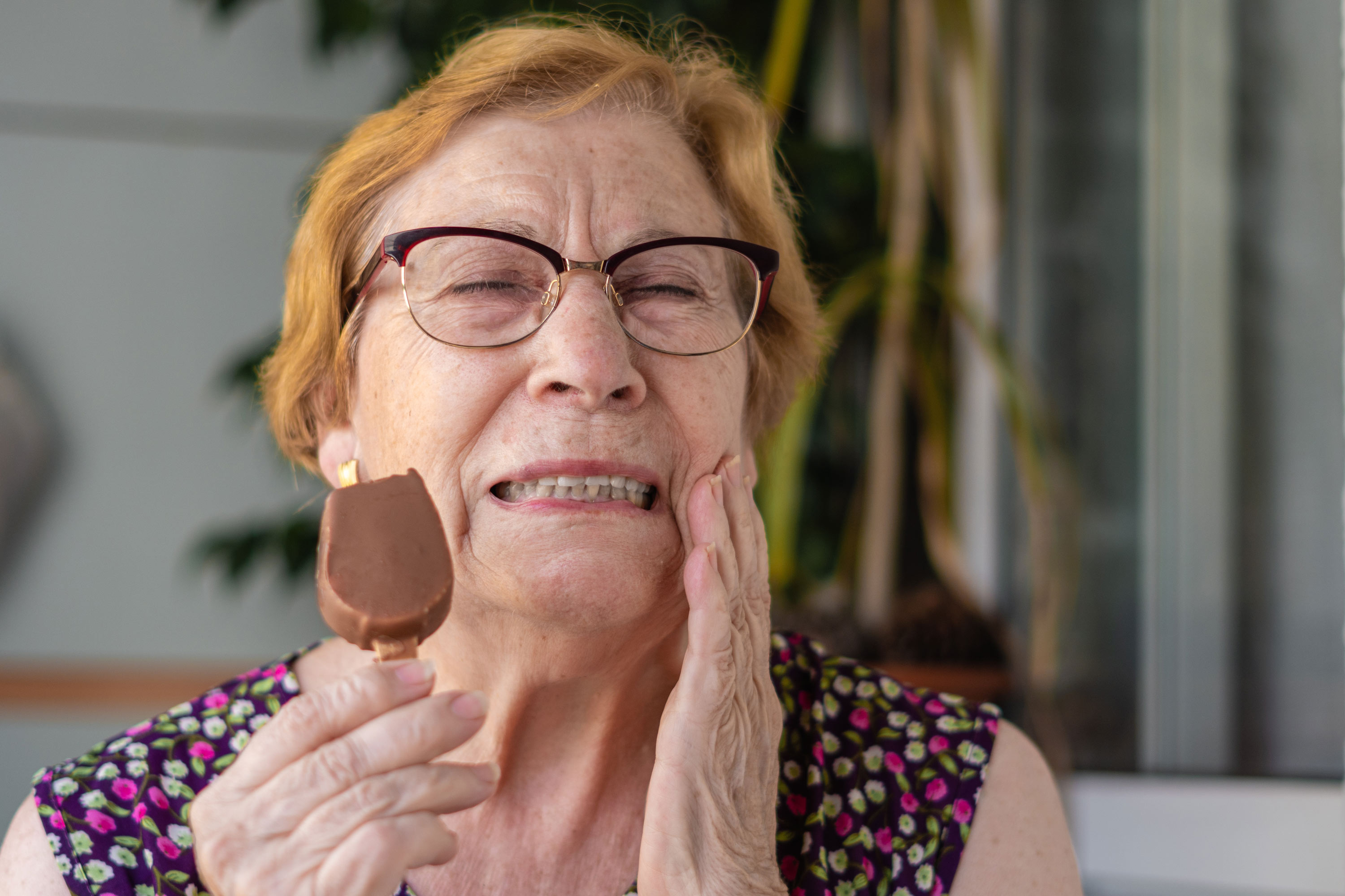 Senior woman eating ice cream bar and holding jaw in pain