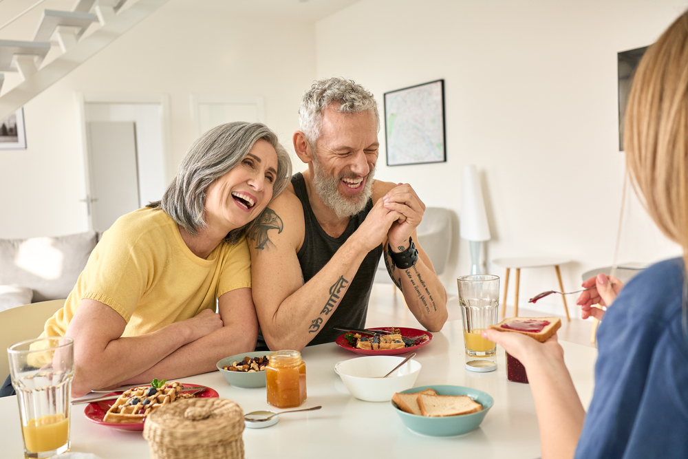 Older couple laughing over breakfast with their young adult daughter