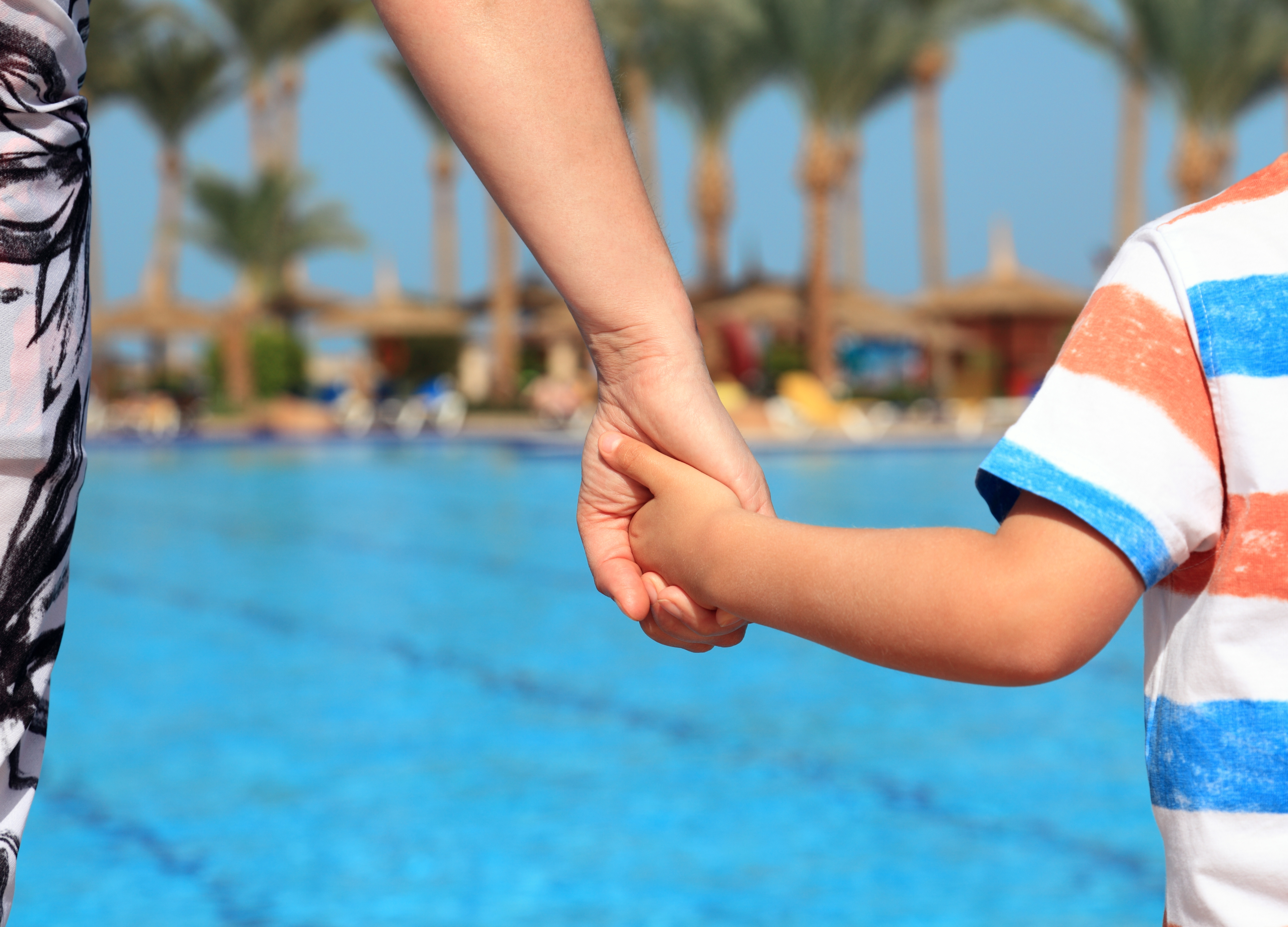 Adult holding a child’s hand beside a swimming pool in California