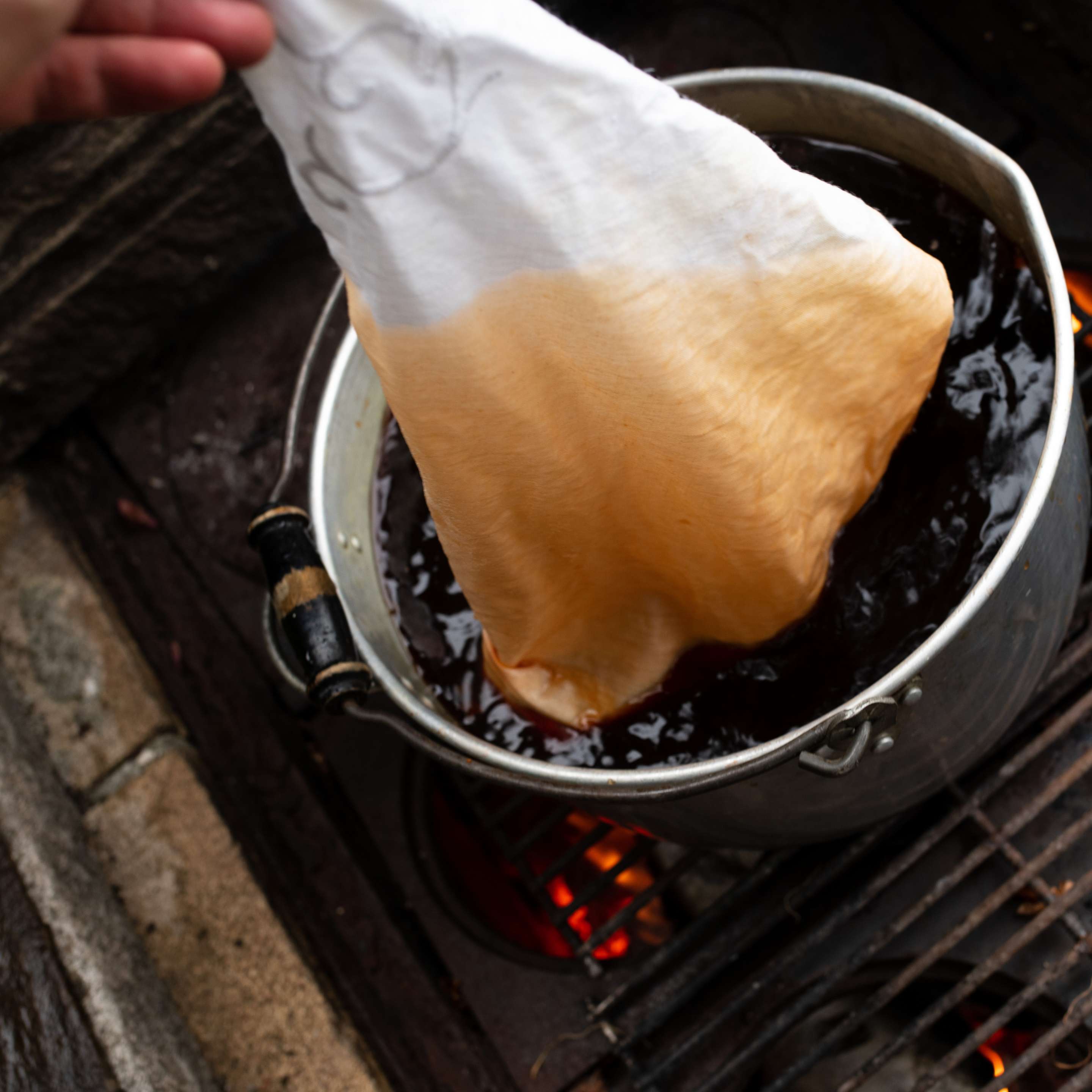 White fabric being immersed in a rich amber onion-skin dye bath