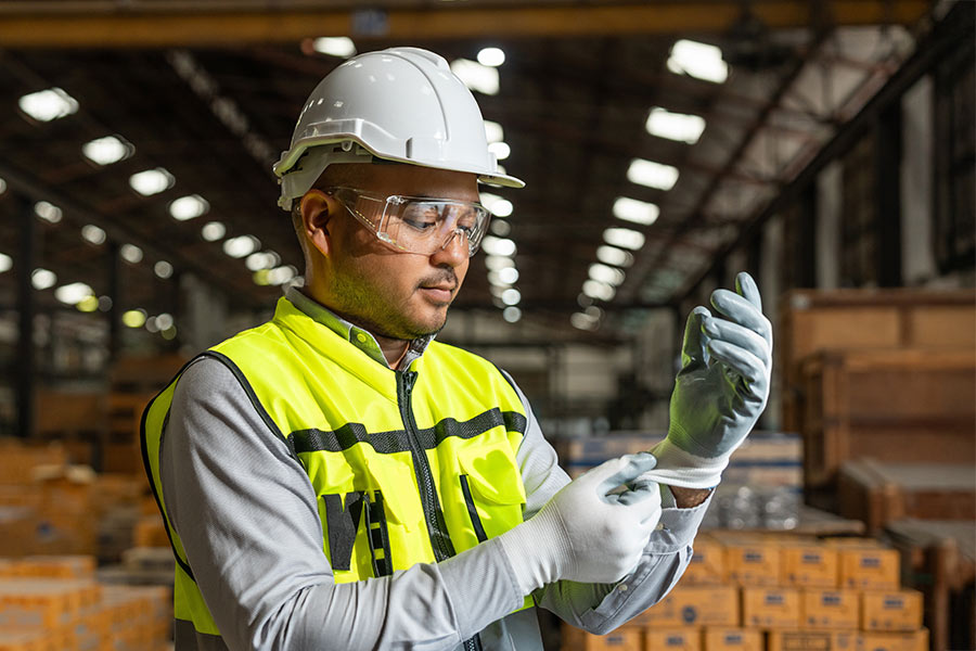 a warehouse worker putting on MRO safety gear - hard hat, safety gloves, eye protection, hi-visibility vest