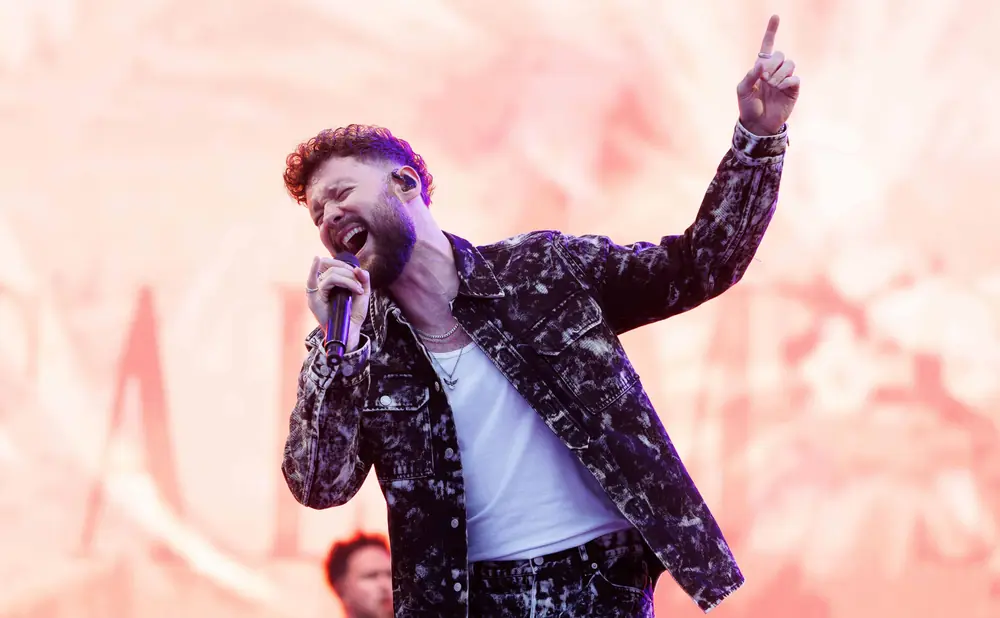 A male singer belts into a microphone while raising his hand in the air.