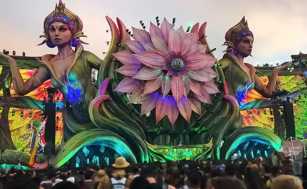 A giant flower stage at an outdoor festival with two large statues of women on either side.