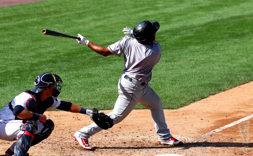 A baseball batter swings at a pitch while a catcher waits behind home plate.