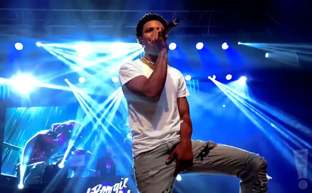 A Boogie Wit Da Hoodie performs on stage with blue lights and a screen behind him.