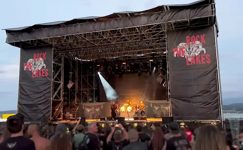 Rock band performing on stage at Rock the Lakes festival, with a crowd in the foreground.