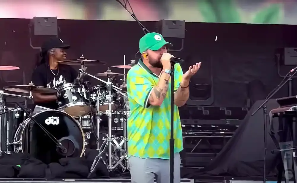 A drummer and a singer perform on a stage, with the drummer on the left and the singer in the center.