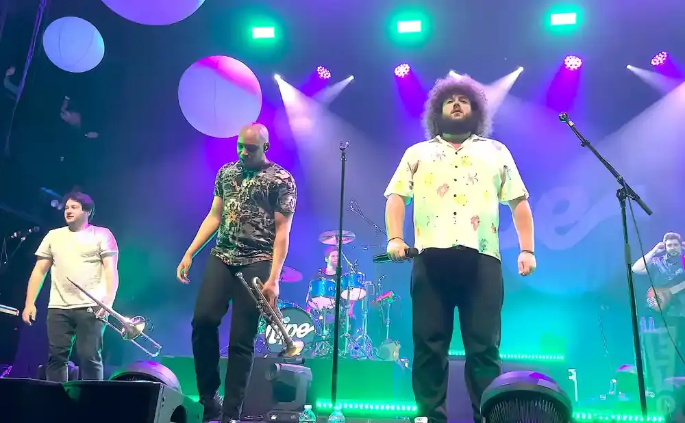 Band members on stage playing instruments under purple and green lights.