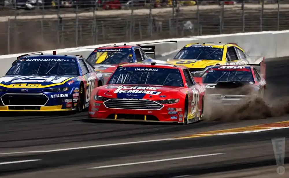 NASCAR race cars in a close pack, kicking up dust on the track.