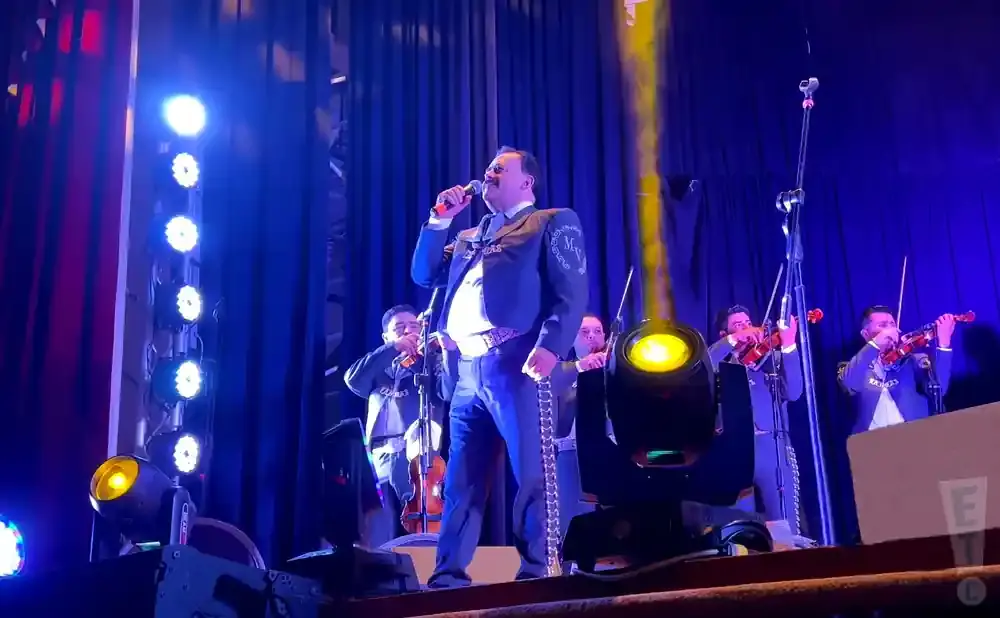 A mariachi singer performs on stage with a band playing violins.