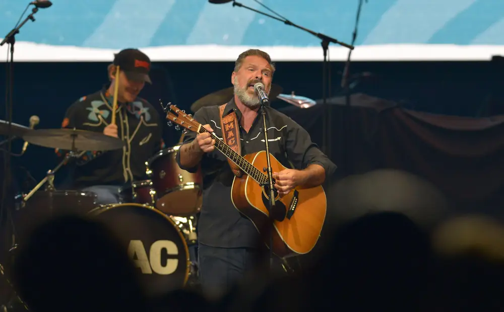 A man with a beard sings and plays an acoustic guitar on stage.