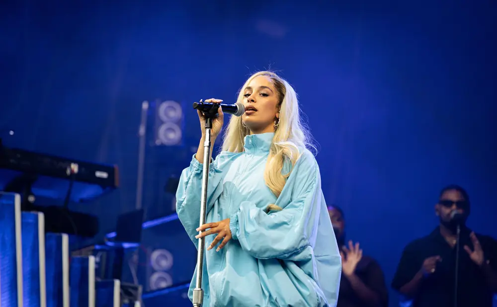 Singer on stage in a blue tracksuit, holding a microphone with a blue background.