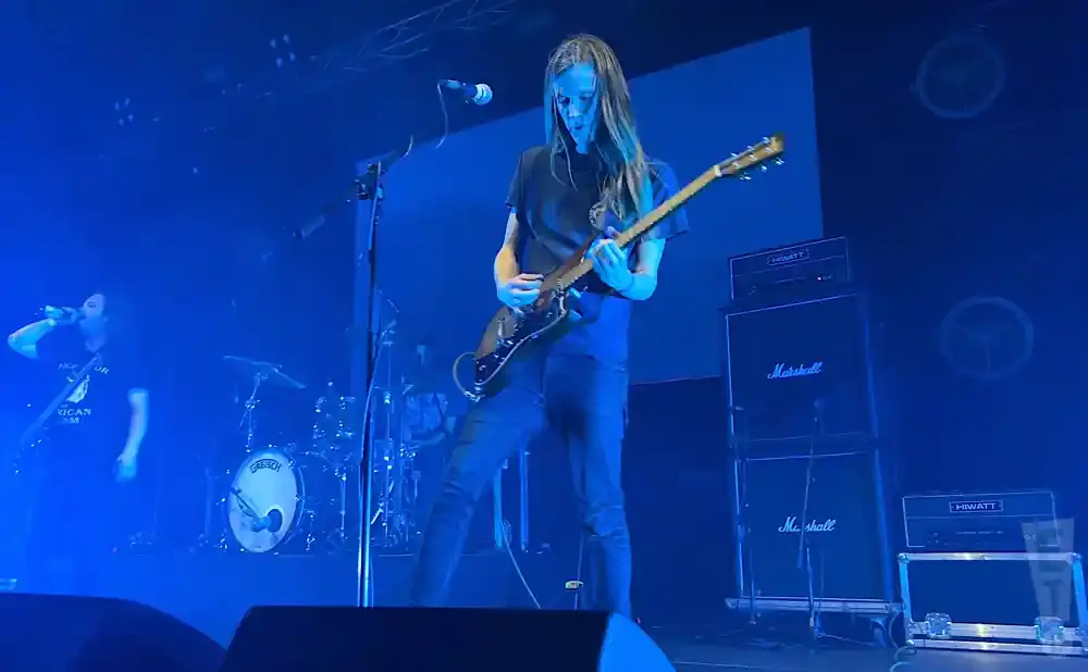 A rock band performs on a stage bathed in blue light, with a guitarist center stage.