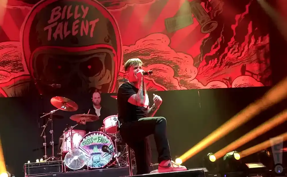 Singer performing on stage with a drummer in the background.