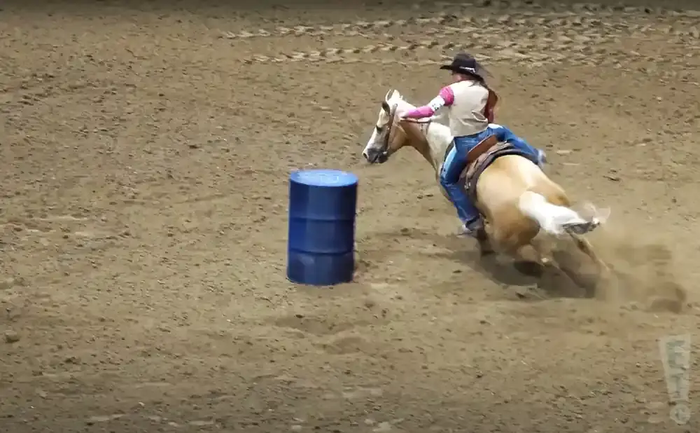 A rider on a horse rounds a barrel in a dusty arena.