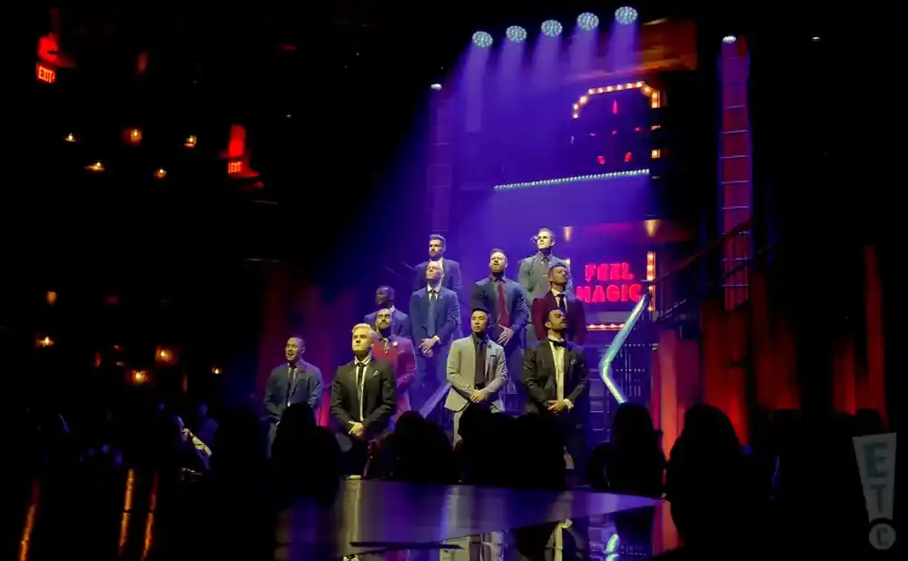 A group of men in suits stand on a stage with dramatic lighting.