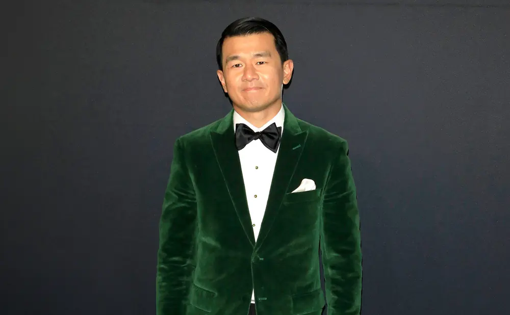 Man in green velvet suit with black bow tie stands against a dark background.