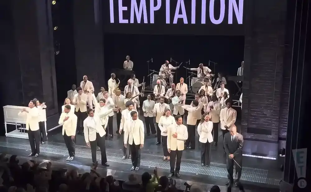 A large ensemble in cream suits performs on stage with 