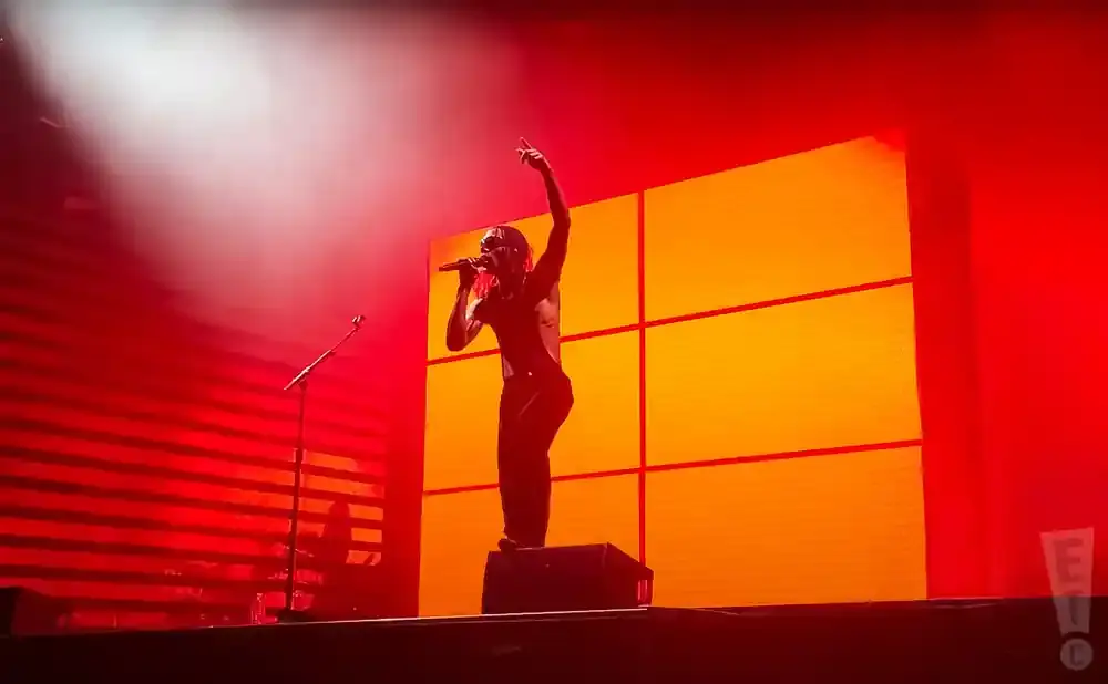 A performer on stage with a microphone, silhouetted against a bright orange and red backdrop.