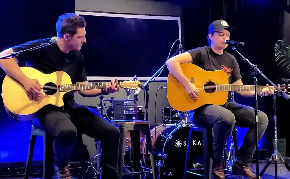 Two men playing acoustic guitars and singing into microphones on a stage.