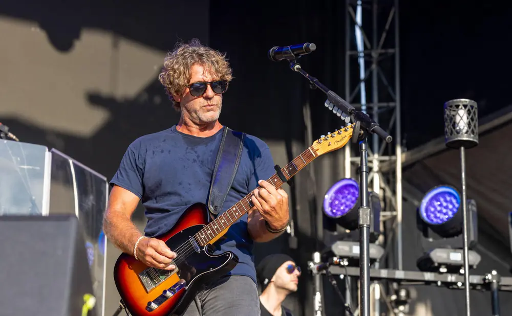 Guitarist plays a sunburst Fender Telecaster guitar on stage under bright lights.