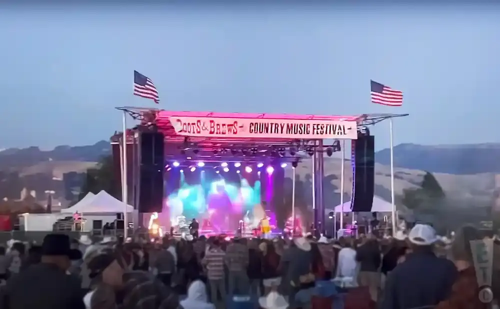 A country music festival stage with American flags and a large crowd gathered.