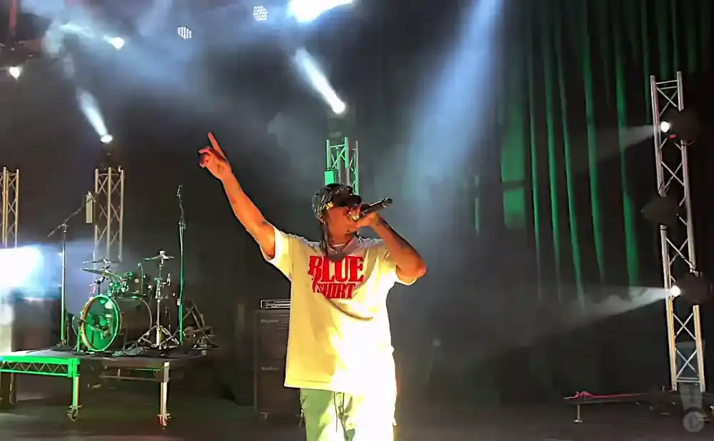 Rapper performing on stage with a drum set and green curtains in the background.