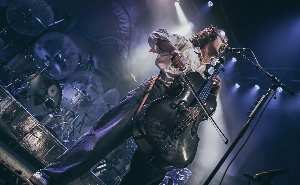 A performer plays a cello on stage with dramatic lighting.