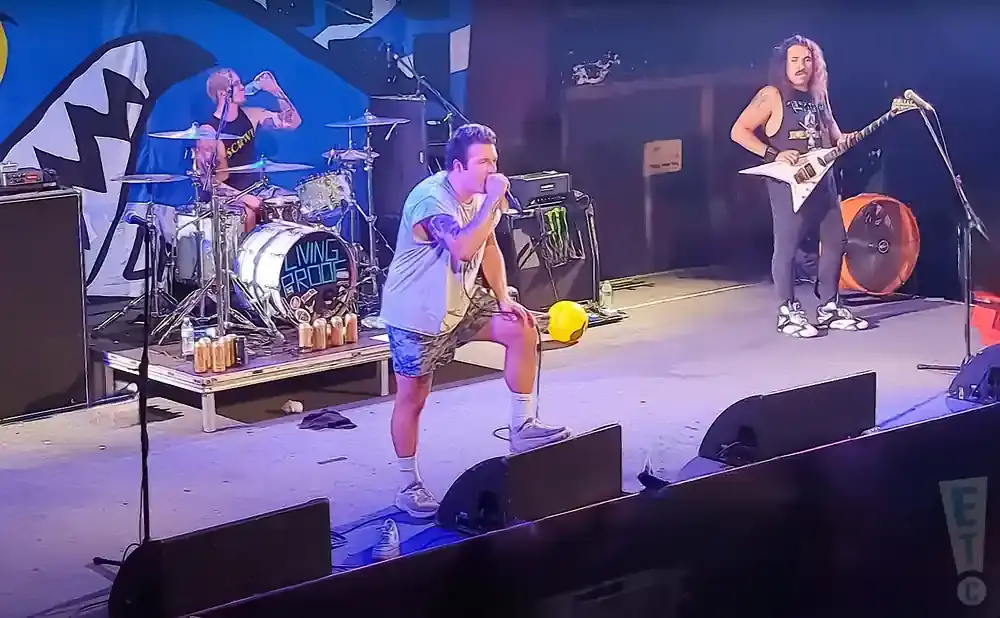 A band performs on stage, with a singer in the foreground and a guitarist and drummer behind him.