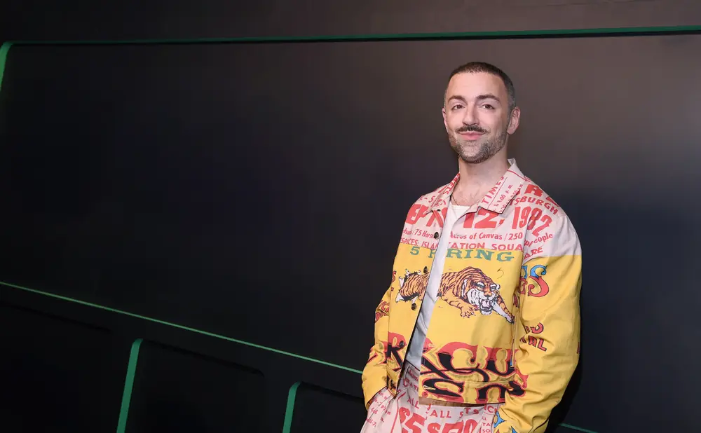 A man in a bold, yellow jacket with tiger graphics and text stands against a dark background.