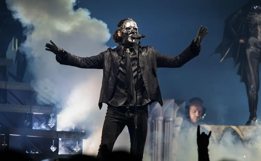 A singer in a skull mask performs on stage with smoke and lights.