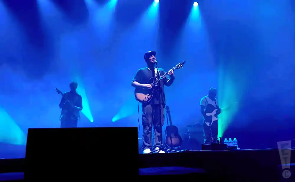 A band plays electric guitars on a blue-lit stage.