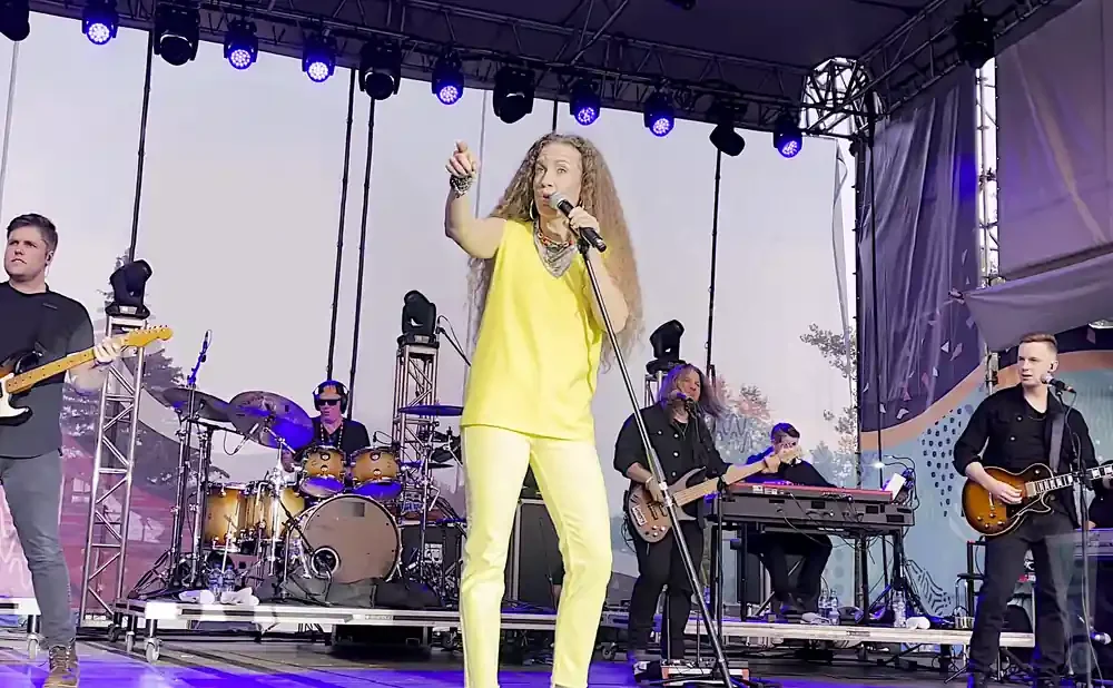 A band performs live on stage, with a female singer in a yellow outfit at the forefront.