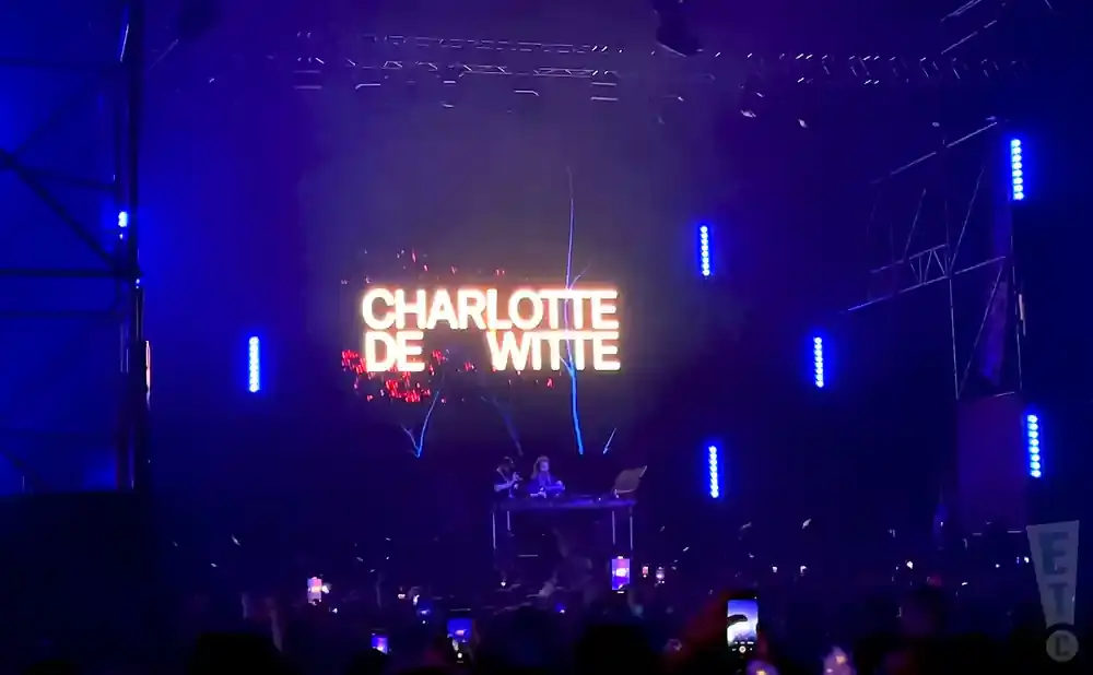 Charlotte de Witte DJing at a concert with neon lights and a crowd below.