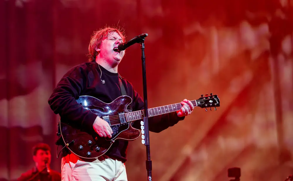 Singer Lewis Capaldi performs on stage, playing a guitar.