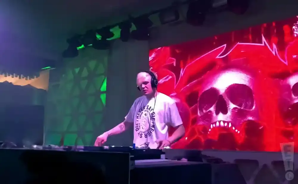 DJ with headphones playing music on turntables, with a large LED screen displaying flaming skulls in the background.