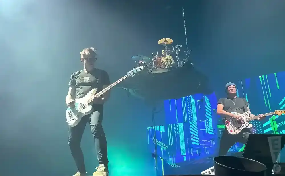 Two guitarists on stage with a drummer on a raised platform behind them.