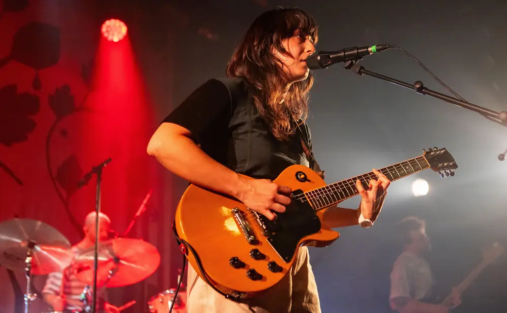 Woman singing and playing a guitar on a dimly lit stage with red spotlights.