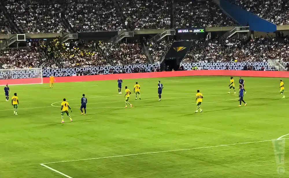 Soccer players in yellow and blue uniforms on a green field during a game, with a crowd in the background.