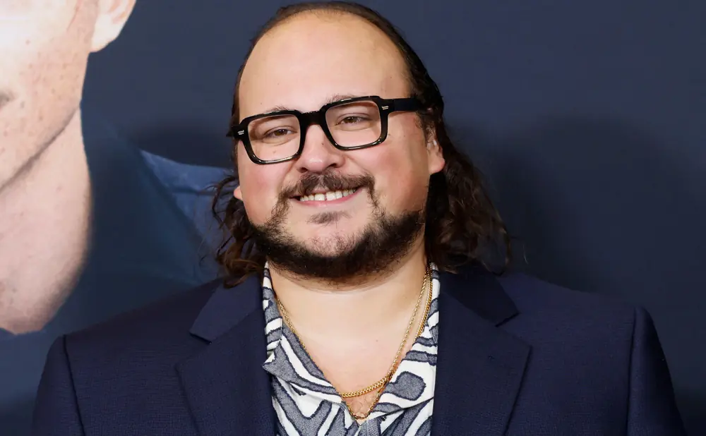 A man with glasses, a beard, and long hair smiles.