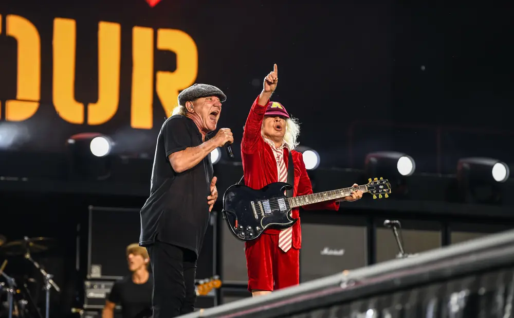 Two male musicians perform on stage, one singing into a microphone, the other playing a guitar.