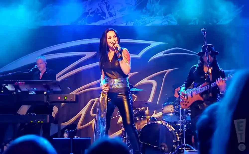 A band performs on stage with a female singer, keyboardist, and bassist under blue lights.