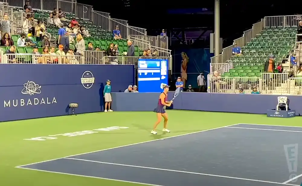 Woman plays tennis during a match with a crowd watching in the stands.
